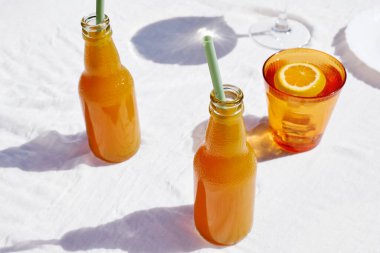 Soğuk yaz içkisi. Masada beyaz masa örtüsüyle pipet içerek taze portakal suyunu şişelerde tazeliyorum..