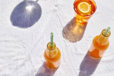 Soğuk yaz içkisi. Masada beyaz masa örtüsüyle pipet içerek taze portakal suyunu şişelerde tazeliyorum..