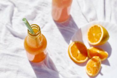 Soğuk yaz içkisi. Masada beyaz masa örtüsüyle pipet içerek taze portakal suyunu şişelerde tazeliyorum..