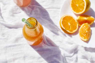 Soğuk yaz içkisi. Masada beyaz masa örtüsüyle pipet içerek taze portakal suyunu şişelerde tazeliyorum..