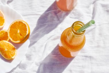 Soğuk yaz içkisi. Masada beyaz masa örtüsüyle pipet içerek taze portakal suyunu şişelerde tazeliyorum..