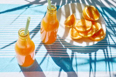 Soğuk yaz içkisi. Taze portakal suyunu şişelerde tazeliyorum. Masada çizgili masa örtüsüyle saman içiyorum..