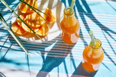 Soğuk yaz içkisi. Taze portakal suyunu şişelerde tazeliyorum. Masada çizgili masa örtüsüyle saman içiyorum..