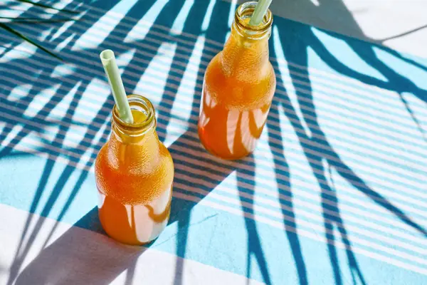 Soğuk yaz içkisi. Taze portakal suyunu şişelerde tazeliyorum. Masada çizgili masa örtüsüyle saman içiyorum..