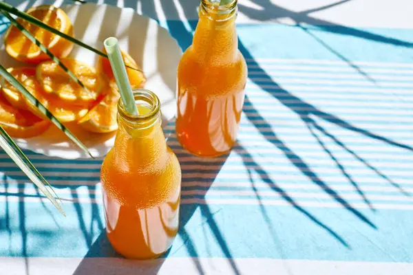 Soğuk yaz içkisi. Taze portakal suyunu şişelerde tazeliyorum. Masada çizgili masa örtüsüyle saman içiyorum..