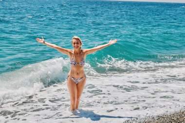 Bikini ve hasır şapka giyen sarışın kadın sahilde eğleniyor.