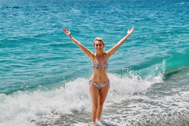 Bikini ve hasır şapka giyen sarışın kadın sahilde eğleniyor.