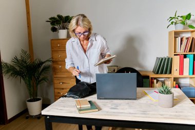 Sarı saçlı iş kadını iş yerine geliyor ve çantasını masanın üstüne boşaltıyor.