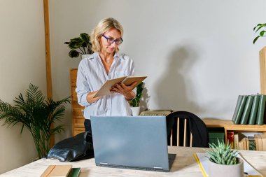Sarı saçlı iş kadını iş yerindeki not defterindeki notları okuyor.