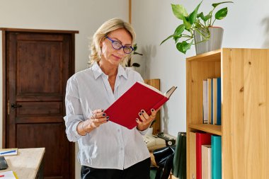 Sarı saçlı iş kadını, ofisteki iş yerinde kitap okurken bilgi arıyor.