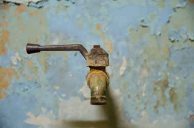 old rusty water tap on pale wall in front view