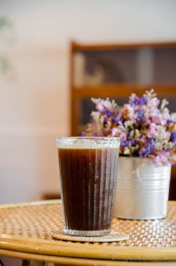 ice americano coffee in tall glass on wooden table with violet flower vase background