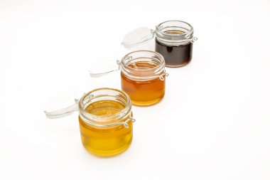 Beyaz arka planda izole edilmiş üç farklı bal çeşidine sahip kavanozlar.