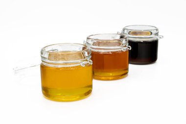 Beyaz arka planda izole edilmiş üç farklı bal çeşidine sahip kavanozlar.