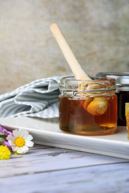 Bal peteğinin yanında farklı bal türleri olan kavanozlar ve yabani çiçeklerle dolu bir tabakta bal kapanı.