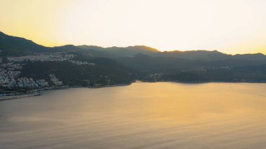 Dağlı güzel deniz manzarası ve turuncu gün batımı gökyüzü. Akşamları tatil köyünün panoraması. Resimli doğa manzarası.
