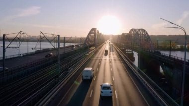 Otoyol köprüsünün arabalı ve demiryolu manzaralı görüntüsü. Parlak akşam gün batımı ışığı.