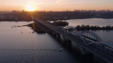 Köprü otoyolu raodunda araba trafiği. Nehrin üzerindeki uzun şehir köprüsü. Parlak akşam gün batımı ışığı.