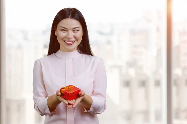 Smiling Asian Woman Giving Red Gift Box Blurred Windows Background — Stok fotoğraf