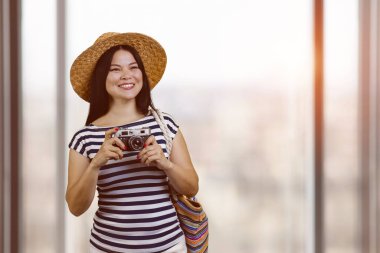 Portrait of happy asian cheerful female tourist with vintage photo camera. Indoor blurred window background.