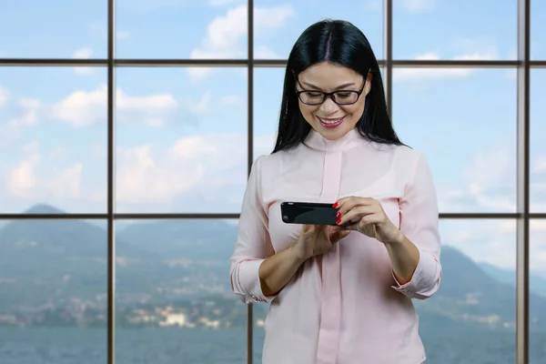 Young asian woman watching a funny video or memes on her smartphone device. Checkered windows background with landscape view.