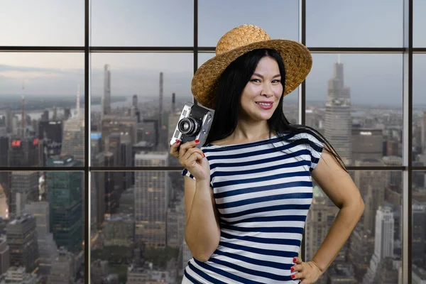 快乐的年轻亚洲女游客拿着一个老式的摄影相机 背景上具有城市景观视图的检查窗口 — 图库照片