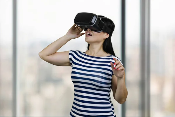 Happy young amazed woman is having virtual reality experience. Blurred windows background.