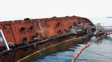 Old rusty overturned oil tanker lying on its edge in the shallow water. Sunken drowned ship after the wreck.