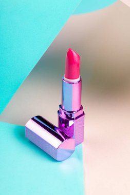 Vertical shot close up of pink lipstick. Reflective purple cap.