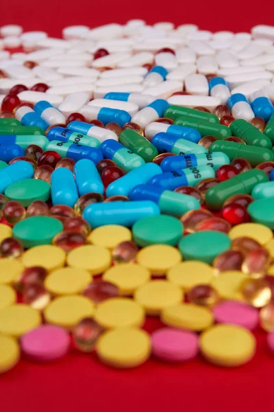 Vertical shot many different colorful medication and pills. Drugs on red background.