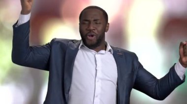 Partide takım elbiseli siyah adam dans ediyor, ağır çekimde. Partide eğlenen ve dans eden Afrikalı bir adamın portresi, renkli bulanık bir arka plan..