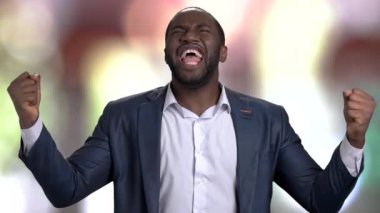 Takım elbiseli mutlu bir zenci zaferi kutluyor. Ağır çekim. Soyut renkli bulanık arkaplan.