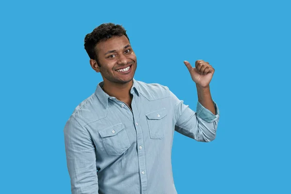 若い笑顔の南アジアの男は親指で後ろを指している 青に隔離された — ストック写真