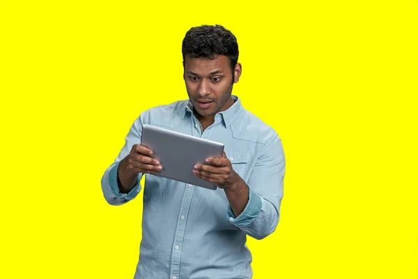 Excited young brown man playing videogame on tablet pc. Isolated on vivid yellow.