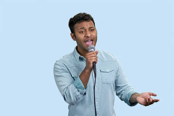 Portrait of a young indian singer with microphone. Southeast asian male on pale blue background.
