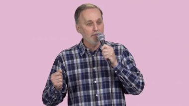 Yaşlı yetişkin bir adam mikrofonla konuşma yapıyor. Pembe üzerine izole edilmiş..