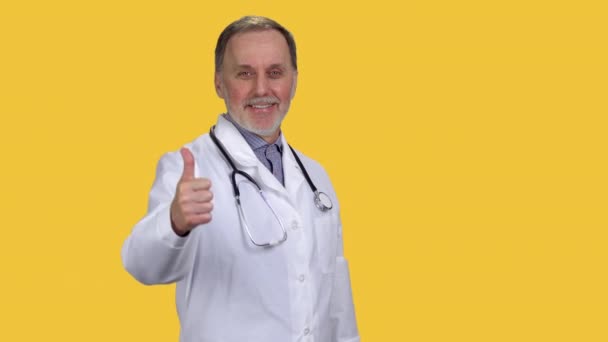 Uśmiechnięty Starszy Lekarz Noszący Stetoskop Podnoszący Kciuk Odizolowane Pomarańczowo — Wideo stockowe