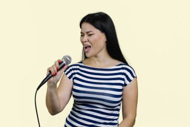 Genç Asyalı kadın mikrofonla şarkı söylüyor. Karaoke 'de mikrofon tutup dans ederken pastel sarısı arka planda poz vermek.