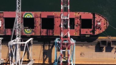 Siyah kömürle dolu bir tankeri boşaltan üç vinç görüntüsü. Deniz limanı lojistiği.