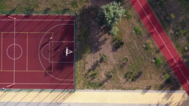 Erkekler kırmızı sahada sokak basketbolu oynar. Havadan üst görünüm.