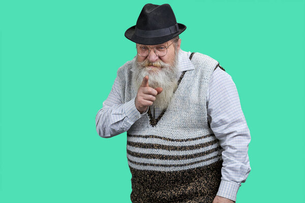 Old bearded man points index finger at camera. Isolated on green background.