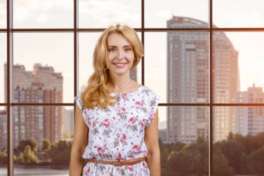 İçerde gülümseyen orta yaşlı bir kadının portresi. Şehir manzaralı işaretlenmiş pencere.