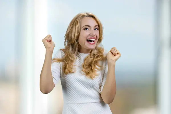 一个快乐而兴奋的金发女人在屋里为某件事感到高兴的画像 背景中模糊不清的窗口 — 图库照片