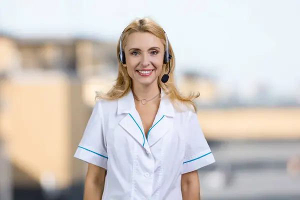 Portrait of smiling blonde woman in headset. Female customer support operator. Blurred outdoor background.