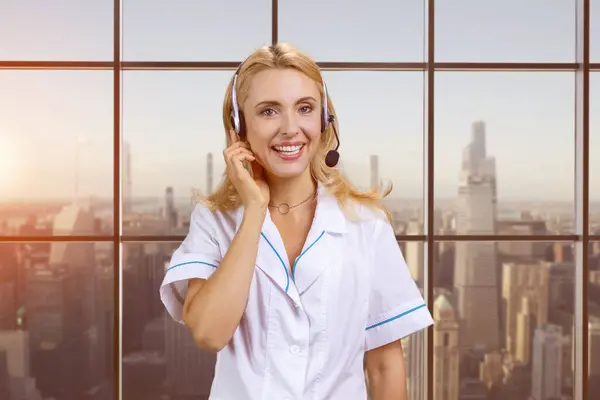 Portrait of happy blonde woman in headset. Female customer support operator. Blurred outdoor background.