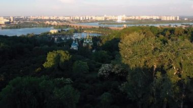 Yeşil parkın, kilisenin, Dnieper Nehri 'nin, köprünün ve şehir binalarının havadan görüntüsü. Kyiv şehir manzarası yukarıdan.