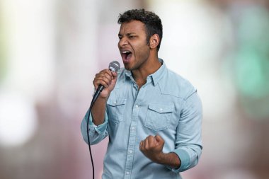Tutkulu erkek şarkıcı en sevdiği şarkıyı söylüyor. Soyut bokeh arkaplanı. Yakışıklı adam tutkuyla şarkı söylüyor..