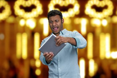 Duygusal, komik, genç bir adam dijital tablette oyun oynuyor. Altın bokeh ışıkları arka plan.