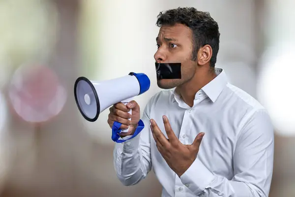口の上に黒いテープを持つ若い男性活動家は メガフォンに話すことができません アブストラクトボケの背景 — ストック写真