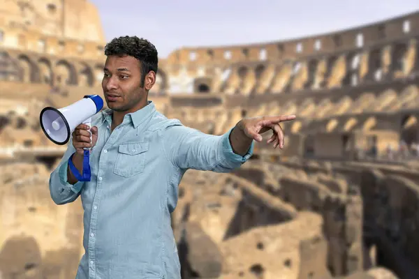 若いインドの男性は イタリアのローマでコロッセオの輝かしい背景に立っている間 メガフォンに話します 古代建築 歴史コンセプト — ストック写真